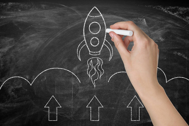 Business startup concept. Woman drawing rocket on blackboard, closeup - Photo, Image