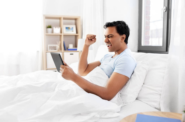 happy indian man with tablet pc in bed at home - Фото, зображення