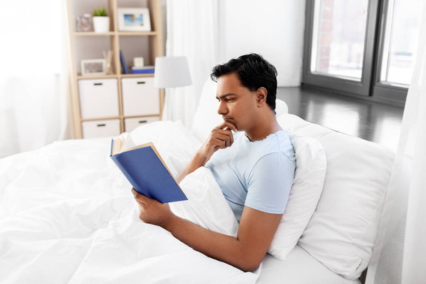 indian man reading book in bed at home - Foto, Imagem