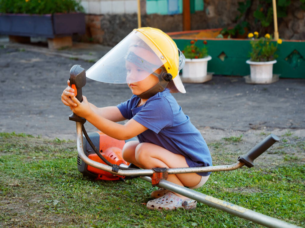 2024 'te çim biçme makinesiyle koruyucu maske takan küçük bir çocuk. - Fotoğraf, Görsel
