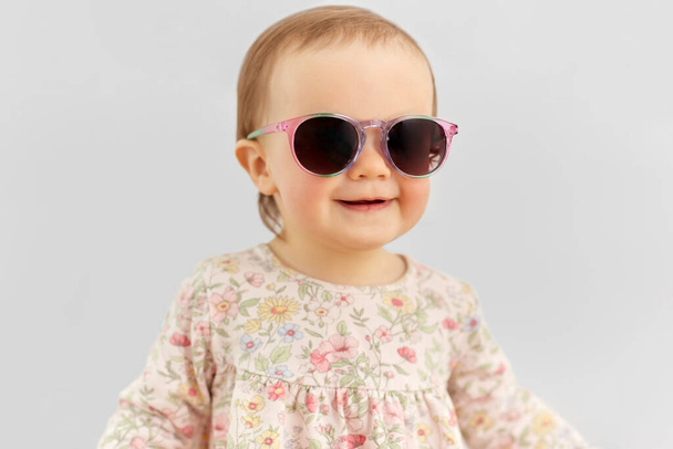 happy little baby girl in sunglasses over grey - Fotoğraf, Görsel