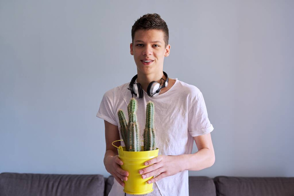 Portrait of teenage boy in headphones holding pot of cacti in his hands - Fotó, kép