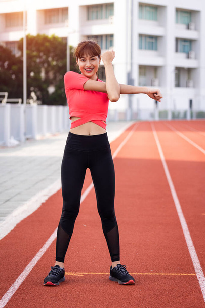 Portrait of a young woman runner warm up and stretching before workout in the morning in city stadium. Healthy and recreation stock photo. - Fotografie, Obrázek