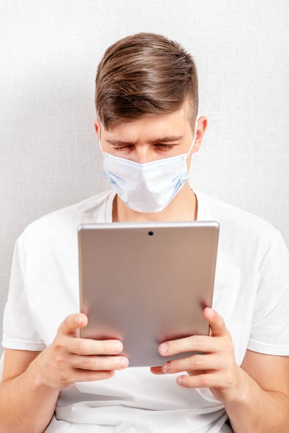 Young Man in Flu Mask with a Tablet by the Wall in the Room - Foto, immagini