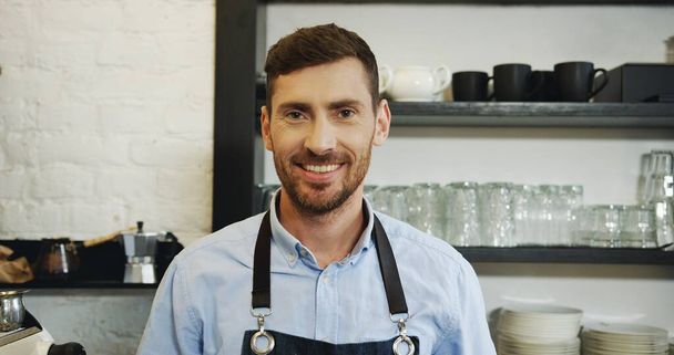 Portrait of the handsome waiter making coffee at the special coffee machine and smiling to the camera. Close up. - Foto, imagen