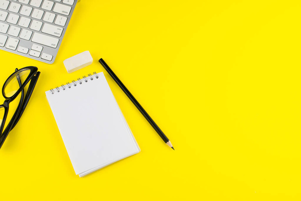 Black eye glasses, pencil, laptop, notepad planner and erase rubber on yellow background. Flat lay. Copy space. Workplace in the office.  - Photo, Image