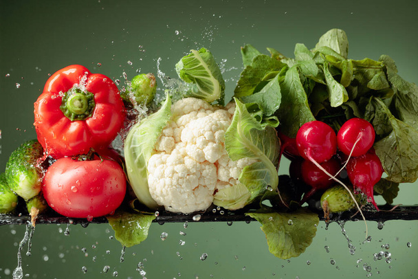 Various raw vegetables with water splash. Cauliflower, tomato, cucumber, radish and paprika on a green background. - Photo, Image