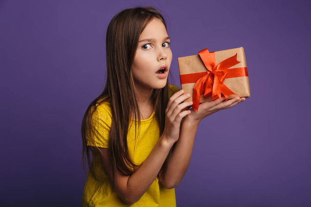 Photo of nice beautiful girl holding gift box and expressing shock isolated over purple background - Photo, image