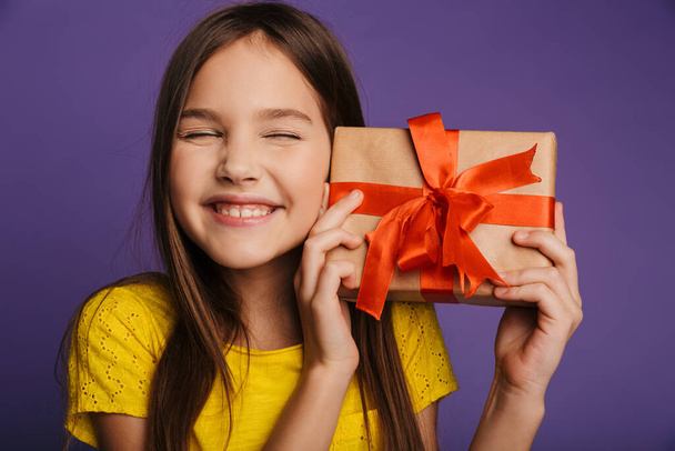 Photo of happy beautiful girl holding gift box and smiling isolated over purple background - Valokuva, kuva