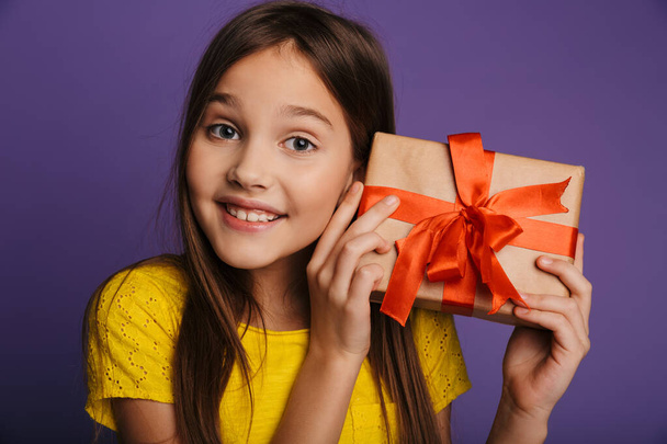 Photo of happy beautiful girl holding gift box and smiling isolated over purple background - Foto, Imagem