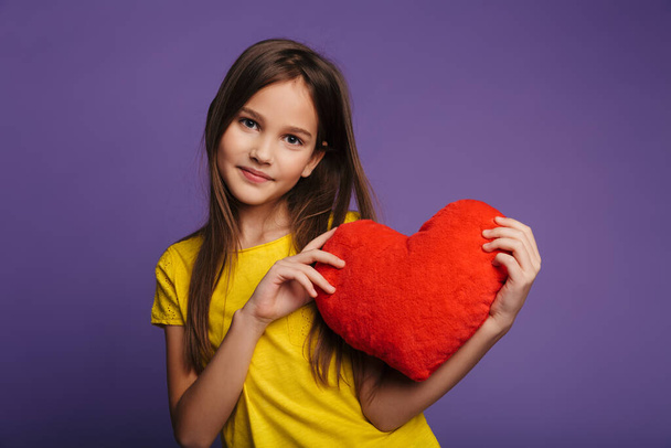 Photo of happy beautiful girl holding soft toy heart and smiling isolated over purple background - Фото, изображение