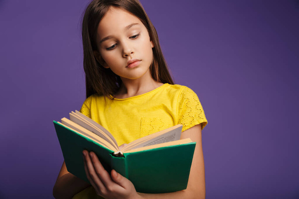 Photo of smart caucasian girl posing and reading book on camera isolated over purple background - Foto, Imagen