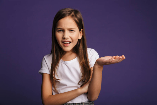 Photo of displeased beautiful girl holding copyspace and looking at camera isolated over purple background - Foto, immagini