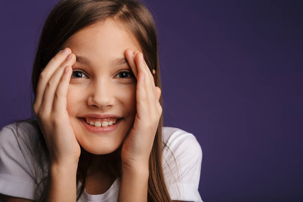 Photo of cheerful beautiful girl covering her face and looking at camera isolated over purple background - Foto, afbeelding
