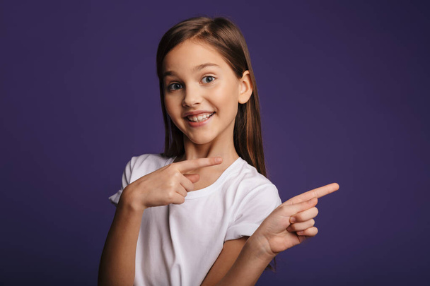 Photo de joyeuse jolie fille souriante et pointant les doigts de côté isolé sur fond violet - Photo, image
