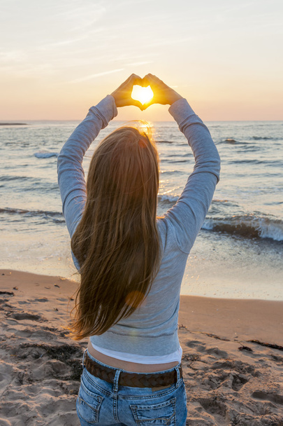 Girl holding hands in heart shape at beach - Foto, Bild