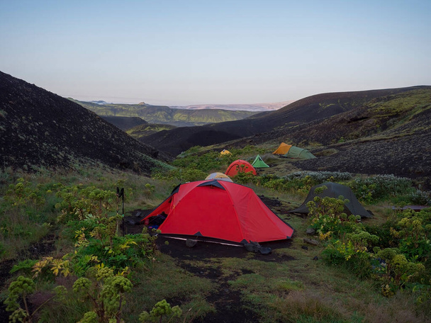 ISLANDE, LANDMANNALAUGAR, 2 août 2019 : Tentes colorées au camping Botnar en Islande sur le sentier de randonnée Laugavegur, vallée verdoyante dans un paysage volcanique au milieu des champs de lave avec vue sur Myrdalsjokull - Photo, image