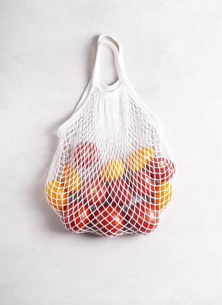 Milieuvriendelijke mesh bag met tomaten op een grijs oppervlak, vlakke lay, bovenaanzicht. Geen afval, geen plastic concept. - Foto, afbeelding