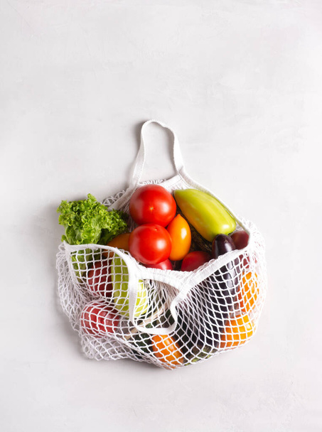 Gri bir yüzey üzerinde sebzelerle çevrili çevre dostu ağ torbası, düz, manzaralı. Sıfır atık. - Fotoğraf, Görsel