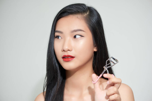 Asian woman corrects eyelashes with curling tongs, close up - Foto, afbeelding