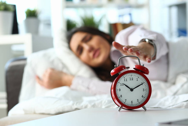 Mujer somnolienta apagando el despertador por la mañana
 - Foto, imagen