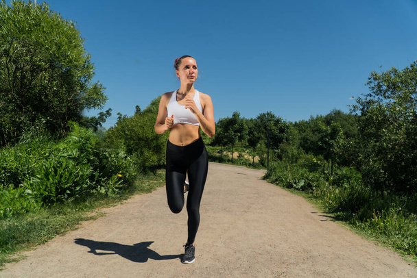 stylish young girl in sportswear runs in a park in the fresh air. The concept of fitness training at sunset in summer, athletics for weight loss, weight loss - Photo, Image