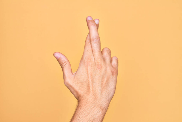 Main de jeune homme caucasien montrant les doigts sur fond jaune isolé gesticulant doigts croisés, superstition et geste chanceux, expression de chance et d'espoir - Photo, image