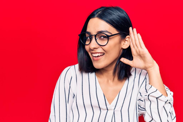 Young beautiful latin woman wearing casual clothes smiling with hand over ear listening and hearing to rumor or gossip. deafness concept.  - Photo, Image