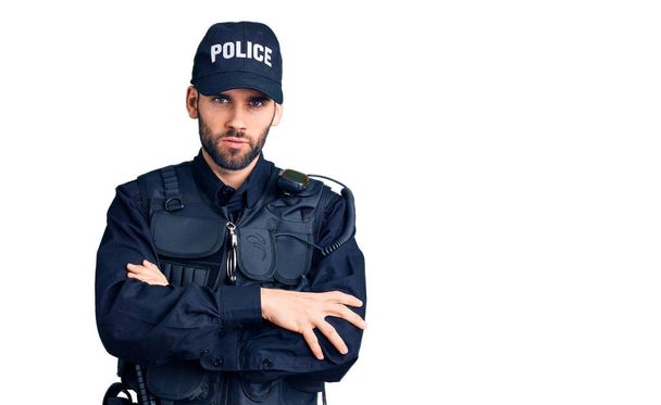 Jonge knappe man met baard draagt politie uniform sceptisch en nerveus, afkeurende uitdrukking op gezicht met gekruiste armen. negatieve persoon.  - Foto, afbeelding
