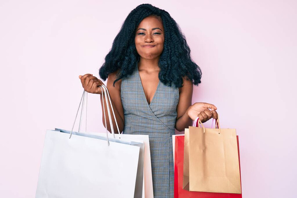 Giovane donna afroamericana con borse della spesa che gonfiano le guance con una faccia buffa. bocca gonfiata con aria, cattura dell'aria.  - Foto, immagini