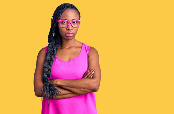 カジュアルな服と眼鏡を身に着けている若いアフリカ系アメリカ人女性は懐疑的で緊張し、交差した腕で顔に不承認の表現。否定的な人.  - 写真・画像