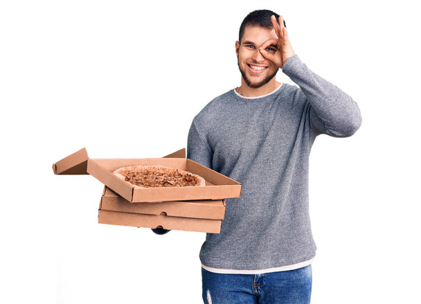 Nuori komea mies tilalla toimitus italialainen pizza laatikot hymyillen onnellinen tekee ok merkki käsin silmästä sormien läpi  - Valokuva, kuva