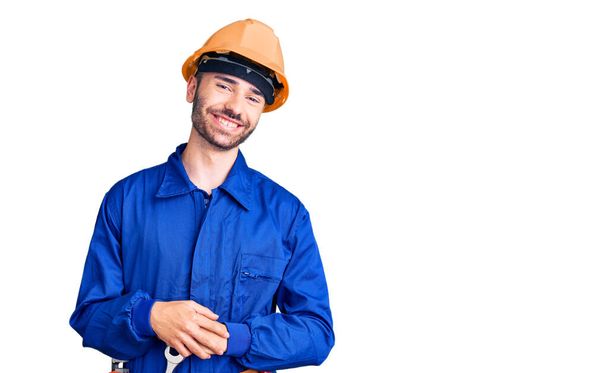 Jeune homme hispanique portant l'uniforme de travailleur avec les mains jointes et les doigts croisés souriant détendu et joyeux. succès et optimisme  - Photo, image