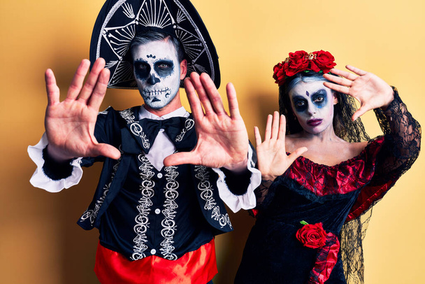 Young couple wearing mexican day of the dead costume over yellow doing frame using hands palms and fingers, camera perspective  - Photo, Image