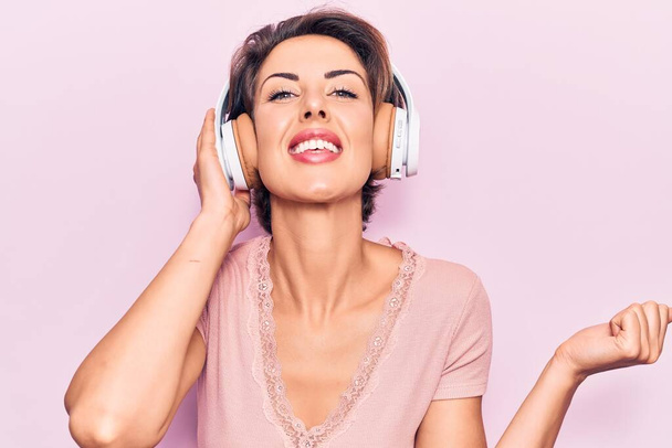 Young beautiful woman listening to music using headphones screaming proud, celebrating victory and success very excited with raised arm  - Fotografie, Obrázek