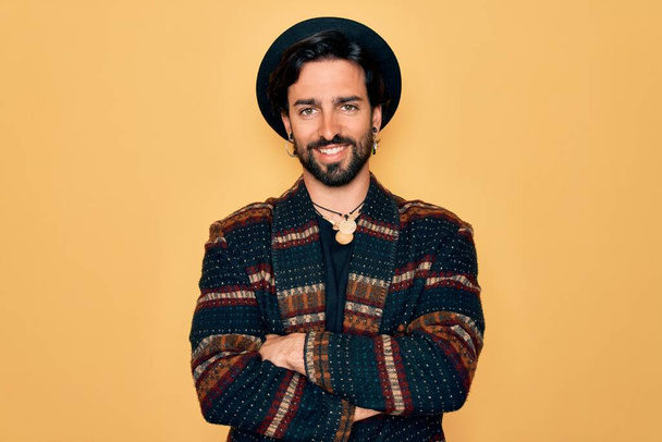 Fiatal jóképű spanyol bohém férfi hippi stílusban és bohókás kalapban boldog arc mosolyogva keresztbe tett karral a kamerába néz. Pozitív személy. - Fotó, kép