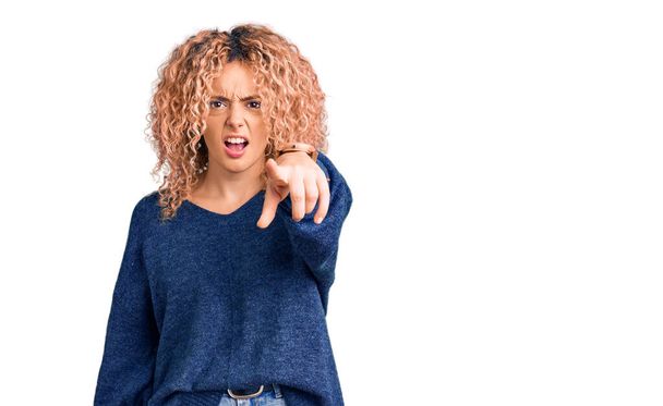 Young blonde woman with curly hair wearing casual winter sweater pointing displeased and frustrated to the camera, angry and furious with you  - Foto, imagen