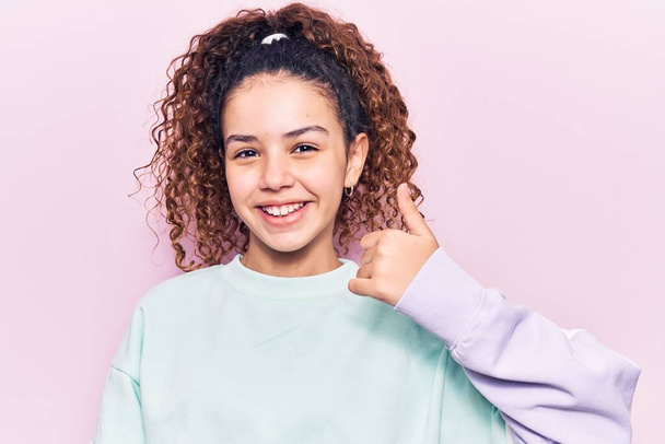 Beautiful kid girl with curly hair wearing casual clothes smiling happy and positive, thumb up doing excellent and approval sign  - Φωτογραφία, εικόνα