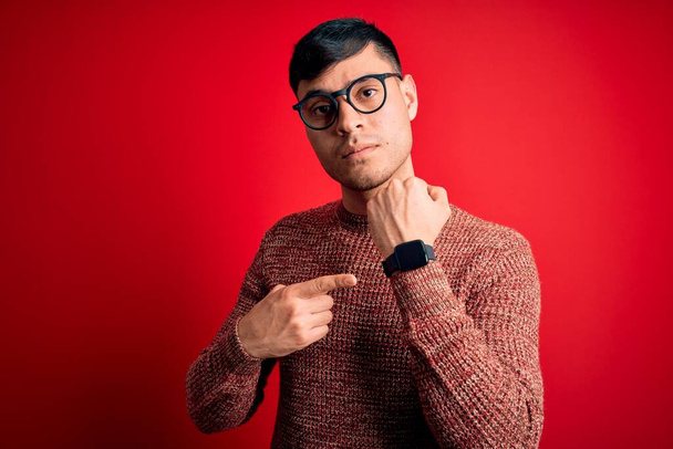 Jovem hispânico bonito vestindo óculos nerd sobre fundo vermelho Com pressa apontando para assistir o tempo, impaciência, olhando para a câmera com expressão relaxada
 - Foto, Imagem