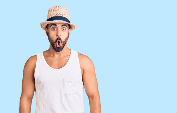 Young hispanic man wearing casual summer hat afraid and shocked with surprise expression, fear and excited face.  - Photo, Image