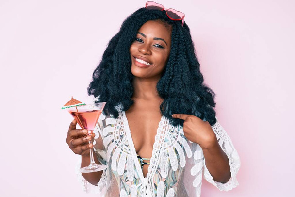Bella donna africana indossa look estivo e bere cocktail puntando il dito verso un sé sorridente felice e orgoglioso  - Foto, immagini