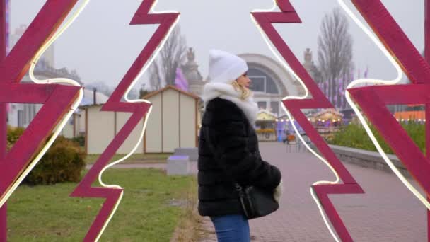 Mujer con sombrero blanco, bufanda, manoplas camina al aire libre en invierno. Ambiente de Año Nuevo
 - Imágenes, Vídeo