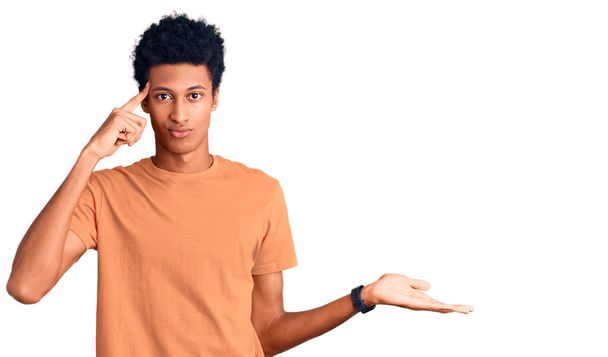 カジュアルな服を着ている若いアフリカ系アメリカ人の男性は、コピースペースを示し、額に指を指すヤシに混乱し、悩まされています。考えてみてください.  - 写真・画像
