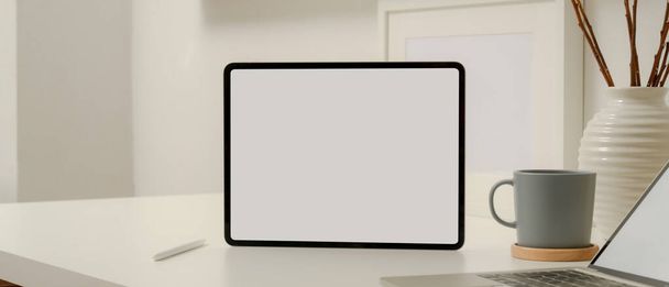 Закройте вид на бланковый экран планшета на белом червонце стилизованным карандашом, ноутбуком, чашкой кофе и украшением  - Фото, изображение