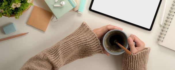 Top view of female student hands holding coffee cup while sitting at worktable with mock up tablet and stationery  - Foto, Imagem