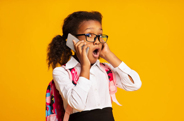 Choqué écolière africaine parlant sur téléphone portable debout sur fond jaune - Photo, image