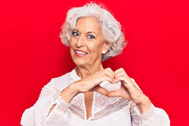 Starsza siwowłosa kobieta w luźnych ciuchach, uśmiechnięta zakochana, robiąca dłońmi kształt symbolu serca. romantyczna koncepcja.  - Zdjęcie, obraz