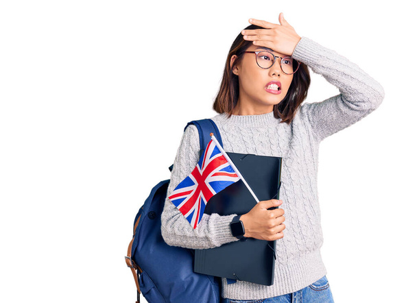 Junge schöne chinesische Mädchen tragen Studentenrucksack mit Ordner und uk Flagge gestresst und frustriert mit der Hand auf dem Kopf, überrascht und wütend Gesicht  - Foto, Bild