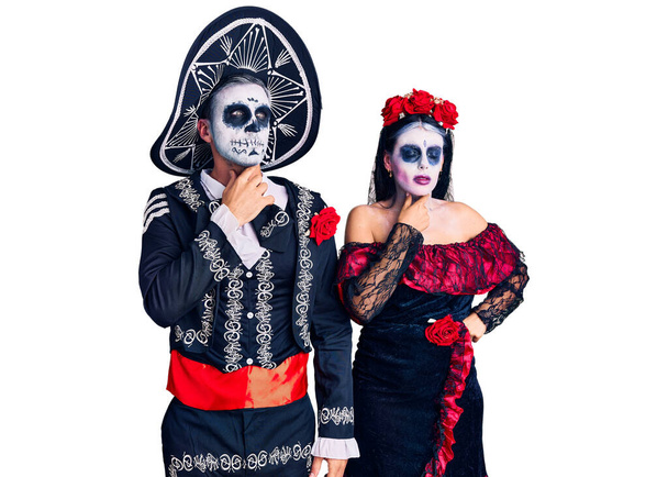 Молодая пара, одетая в мексиканский день мертвого костюма на заднем плане, трогает болезненную шею, болит горло от гриппа, заноз и инфекция  - Фото, изображение