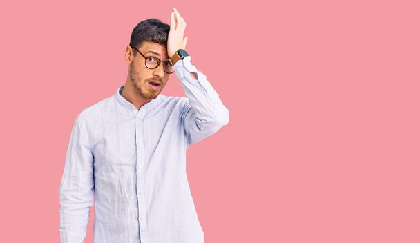 Handsome young man with bear wearing elegant business shirt and glasses surprised with hand on head for mistake, remember error. forgot, bad memory concept.  - Foto, imagen